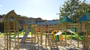 A playground with various play structures including slides and climbing areas, surrounded by sand and grass. - 5 Star Holiday Home in Grindsted (Grindsted)