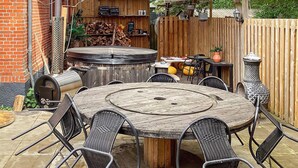 Une terrasse extérieure avec une table et des chaises en bois rondes, un barbecue et une clôture en bois.