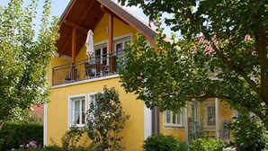 Un bâtiment jaune doté d’un balcon, entouré d’une végétation luxuriante et d’un jardin bien entretenu.