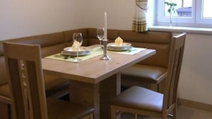 Un coin repas avec une table dressée pour deux personnes, un luminaire suspendu et une fenêtre avec des rideaux.