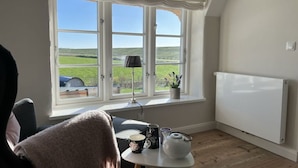 Ein Zimmer mit großem Fenster, Heizkörper, kleinem Tisch mit Teekanne und Stuhl.