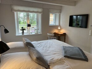 A bedroom with a bed, a desk, a chair, a TV, and windows with curtains. - "peerboos" in the Haus am Deich (Vollerwiek)