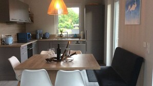 Una cucina moderna con zona pranzo, che include un tavolo in legno, due sedie bianche, una panca nera e una lampada a sospensione.