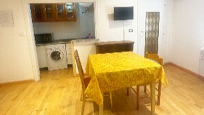 A dining area with a table and chairs, a kitchen in the background, and a television mounted on the wall. - 1 Bedroom Apartment in Alghero (Alghero)