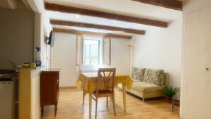 A spacious room with a wooden floor, a dining table with chairs, a sofa, and a small plant. - 1 Bedroom Apartment in Alghero (Alghero)
