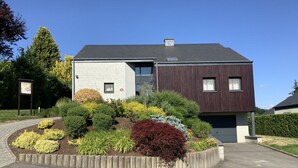 Une maison moderne à deux étages, dotée d’un jardin aménagé à l’avant.