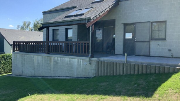 Une maison moderne à deux étages, dotée d’un porche couvert, d’une cour clôturée et offrant une vue sur un ciel dégagé.
