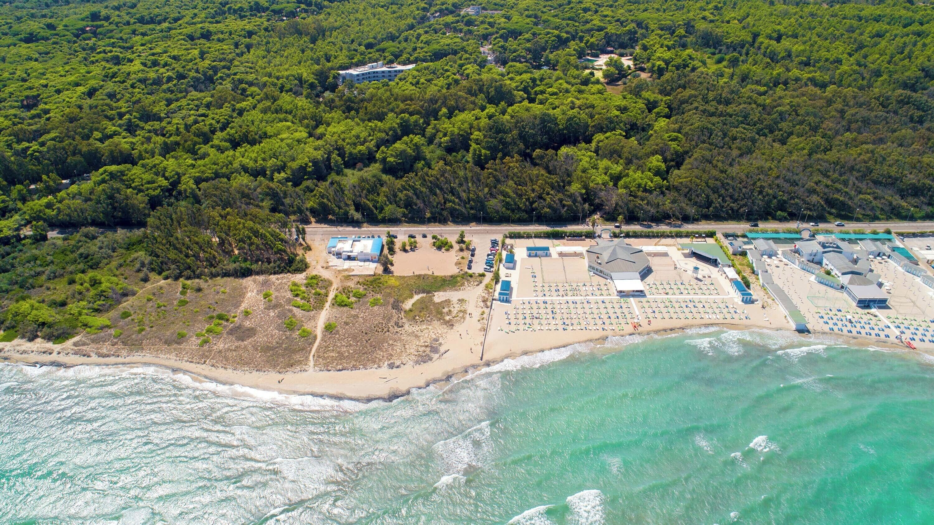 Eine Luftaufnahme eines Küstenresorts mit Strand, Parkplatz und einem großen Gebäude mit mehreren Bereichen.