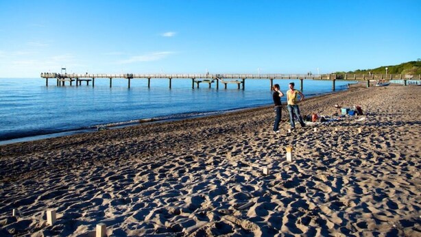 A beach with a pier extending into the water, a sandy shore, and a few people standing near the water's edge. - Chudzik Modern Retreat (Rerik)