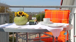 A balcony with a table set for two, a vase with yellow flowers, a cup, and a plaid cushion. - Chudzik Modern Retreat (Rerik)