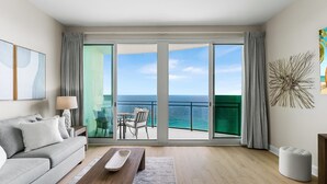 Un salon moderne avec un canapé, une table basse et une vue sur l’océan grâce à de grandes portes coulissantes.