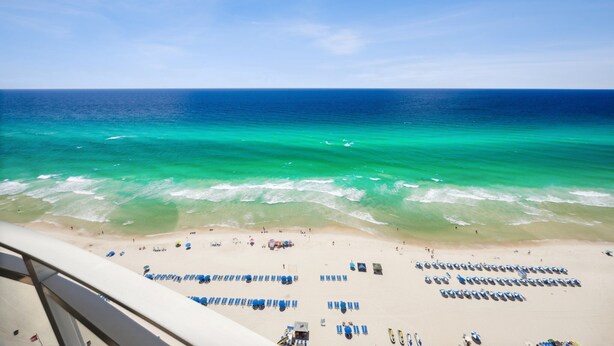 Une plage bordée de rangées de chaises longues et de parasols bleus, une étendue de sable et l’océan.