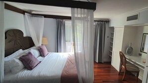 Een slaapkamer met een hemelbed, een bureau met stoel, en een raam met gordijnen.