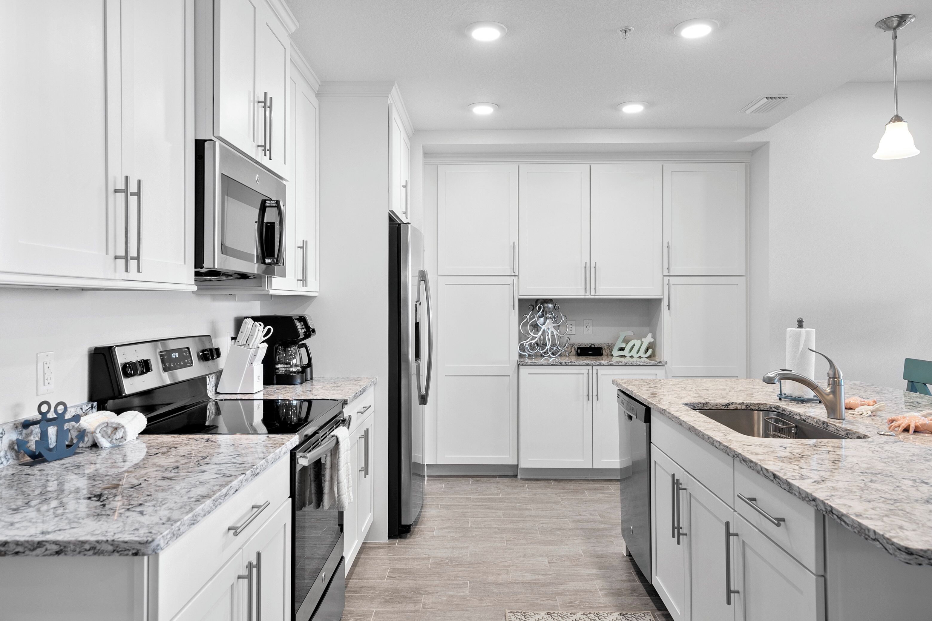 A modern kitchen with white cabinets, stainless steel appliances, granite countertops, and a built-in oven.