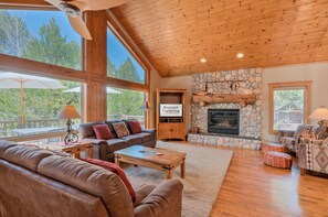 A spacious living room with a stone fireplace, large windows, and a wooden ceiling. - Luxury 6 En Suites, A/C, 14 SHARC, H/T, Bikes, BBQ (Sunriver)