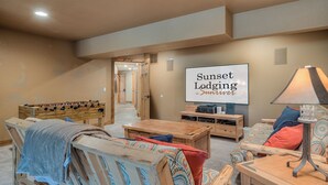 Un saló confortable amb una taula de futbolí, una televisió que mostra 'Sunset Lodging in Summer' i una làmpada sobre una taula de fusta.
