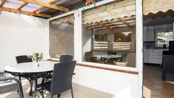 Un patio exterior con una mesa y sillas, un vidrio que da a la cocina y una estructura de techo de madera.