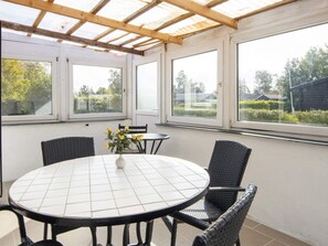 A covered patio with a round table and chairs, large windows, and a view of the outdoors.
