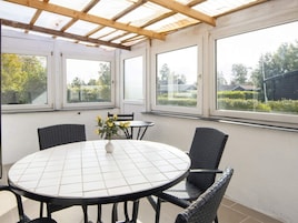 Un patio techado con una mesa redonda y sillas, ventanas amplias y vistas al exterior.
