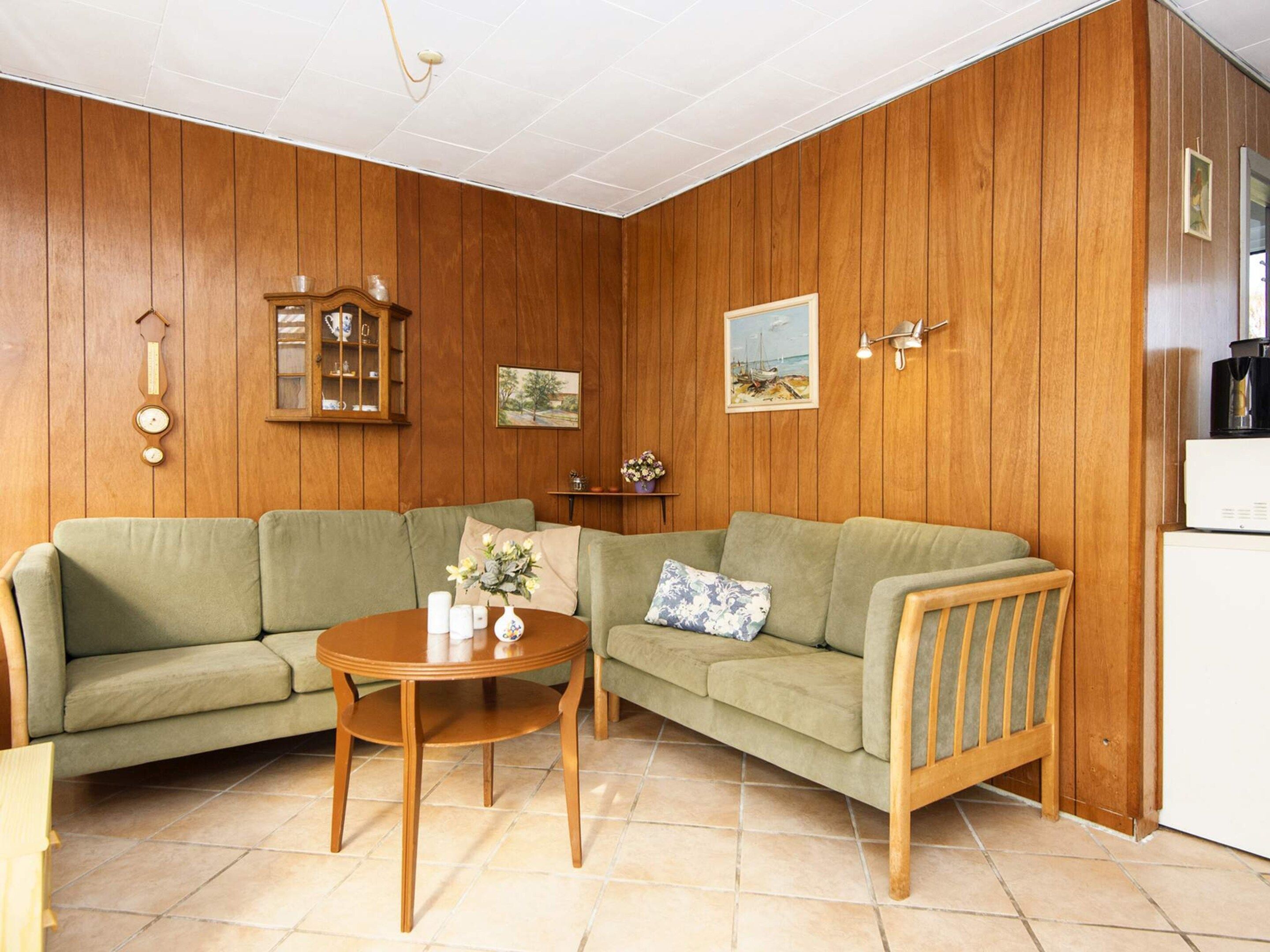 Un salón con un sofá verde, una mesa de centro de madera, un reloj y un cuadro en la pared.
