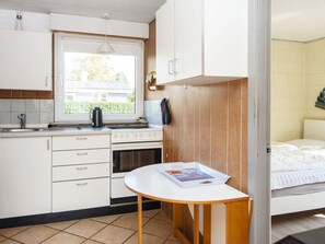 Une petite cuisine avec une fenêtre, une cuisinière et une petite table sur laquelle est posé un magazine.