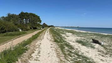A sandy path leading to a beach with a bench and wind turbines in the distance.