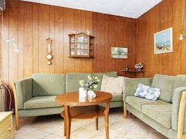 Una habitación con paredes de madera, un sofá verde, una mesa de madera con un florero, un reloj y un cuadro.