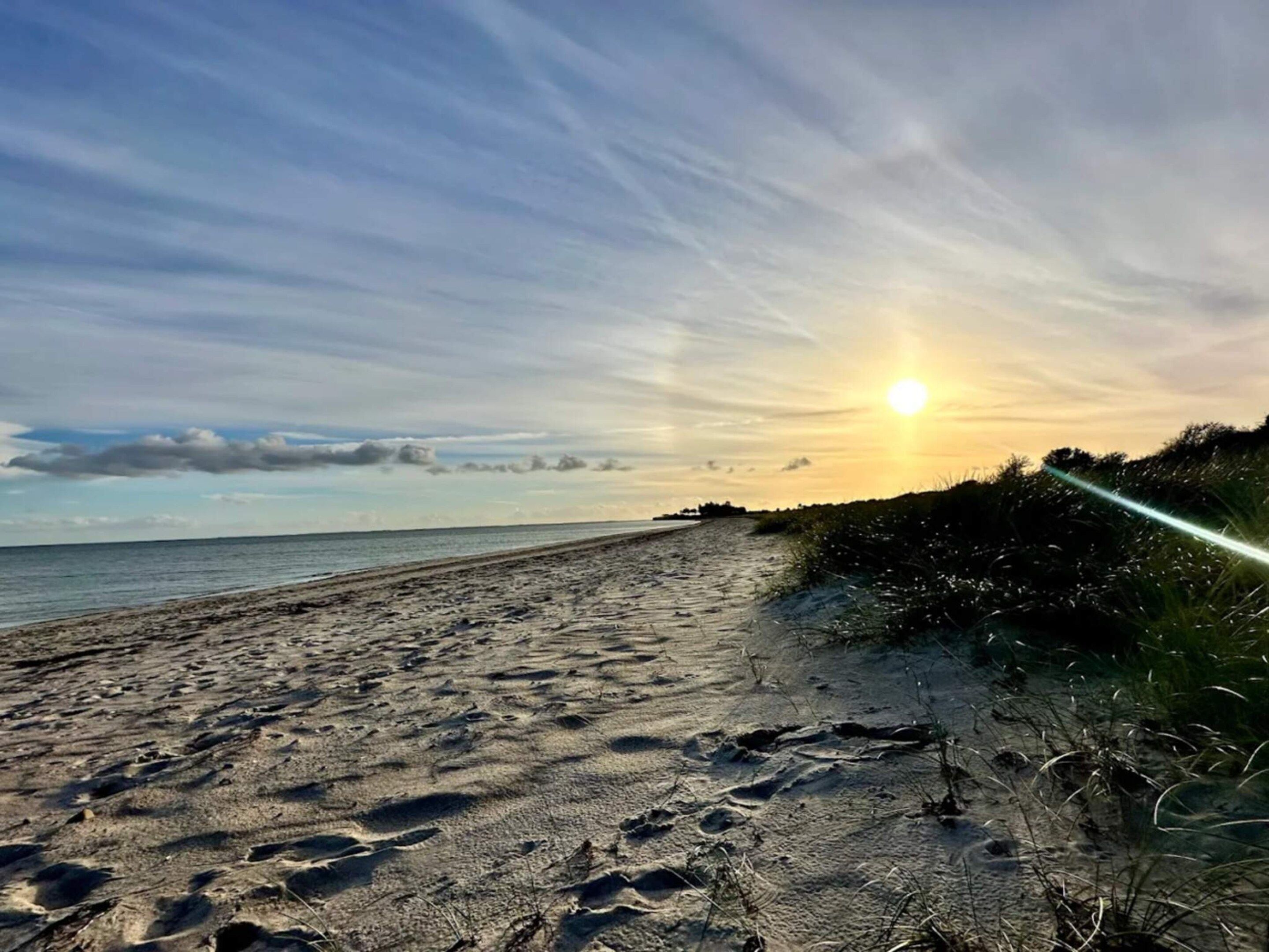 Una playa con huellas en la arena y una puesta de sol al fondo.