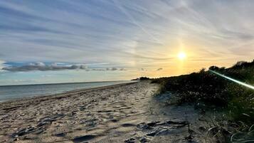Una playa con huellas en la arena y una puesta de sol al fondo.