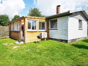 Une petite cabane en bois à l’extérieur blanc, avec une cheminée et un climatiseur mobile.