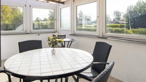 A covered patio with a round table and four chairs, large windows, and a view of the outdoors. - 3 Person Holiday Home in Sydals (Sydals)