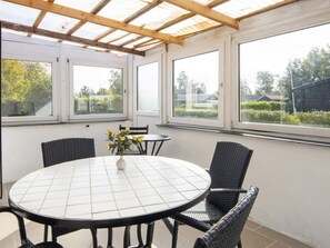 Une terrasse couverte avec une table ronde et quatre chaises, de grandes fenêtres et une vue sur l’extérieur.