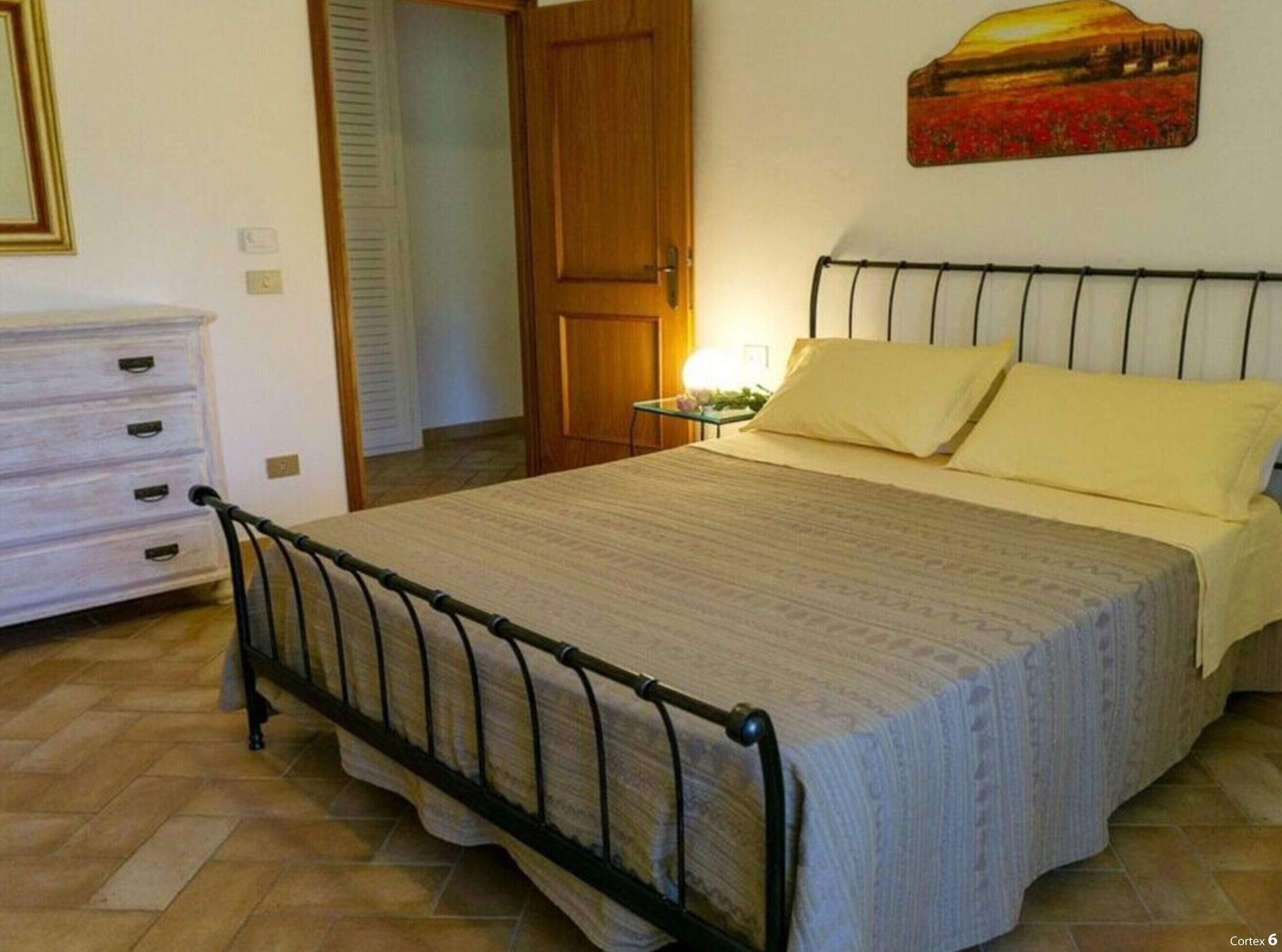 Een slaapkamer met een bed, nachtkastje, dressoir en een deur naar een andere kamer.