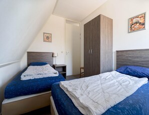 A bedroom with two beds, a wardrobe, a bedside table with a lamp, and a framed picture on the wall.