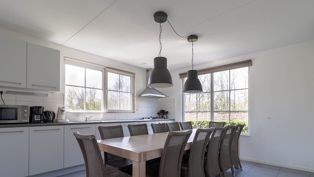 Una cocina moderna con armarios blancos, una mesa de comedor con sillas de mimbre y ventanas amplias.