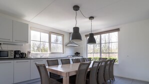 Una cocina moderna con armarios blancos, una mesa de comedor con sillas de mimbre y ventanas amplias.