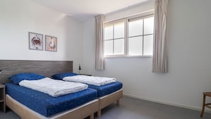 Un dormitorio con dos camas, una mesita de noche, una lámpara y una ventana con cortinas.