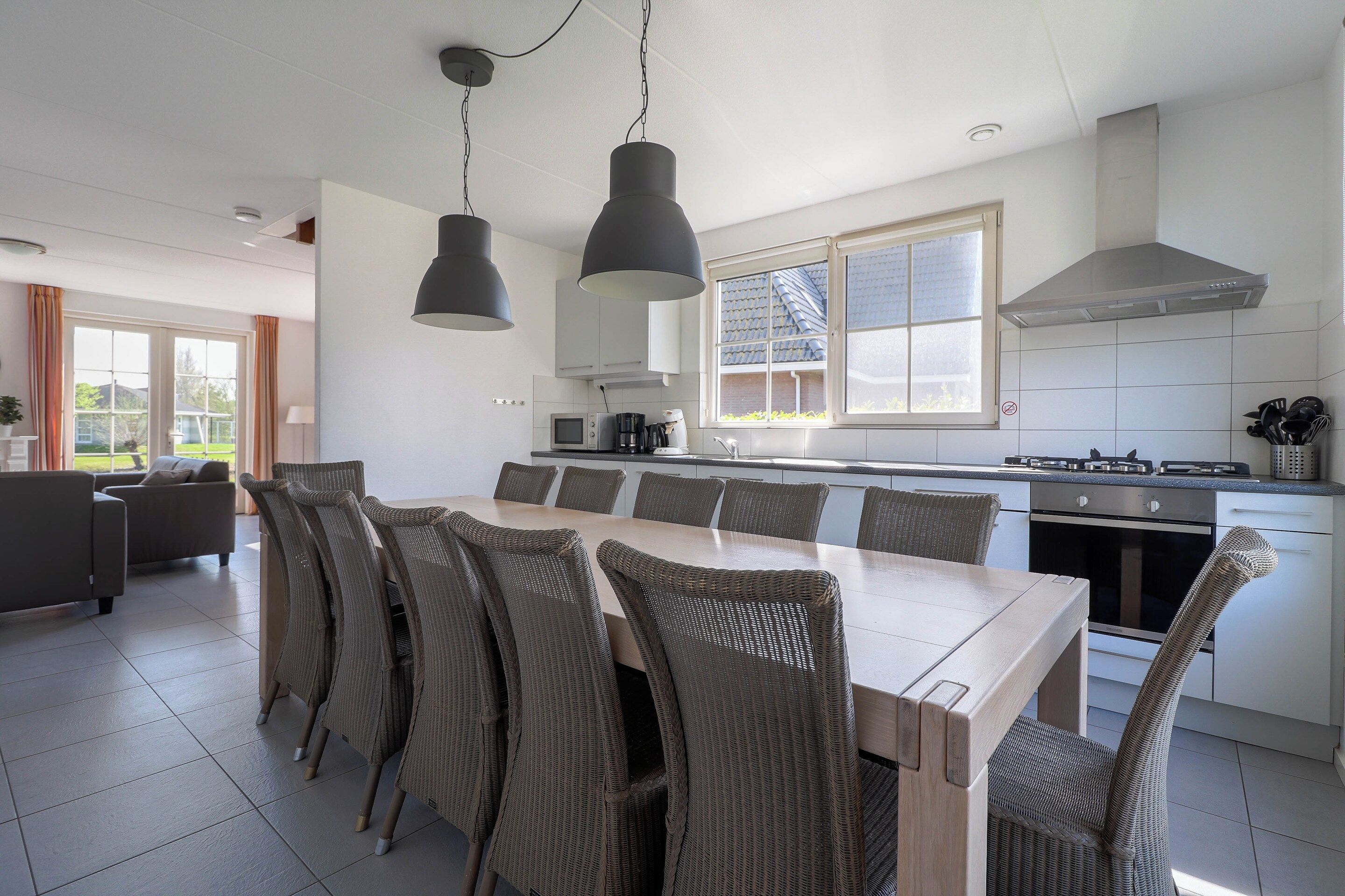 A modern kitchen with a dining area, featuring a large island, overhead lighting, and a view of the outdoors.
