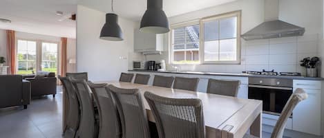 A modern kitchen with a dining area, featuring a large island, overhead lighting, and a view of the outdoors.