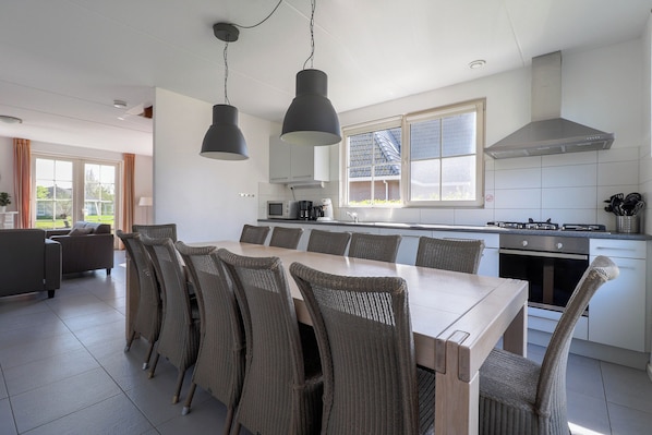 A modern kitchen with a dining area, featuring a large island, overhead lighting, and a view of the outdoors.