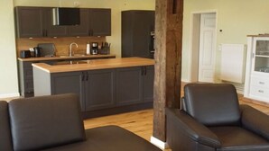 A modern kitchen with dark cabinets, a wooden countertop, and a built-in stove. There are two black leather sofas and a wooden pillar in the center. - Nice Apartment in Klein Upahl (Klein Upahl)