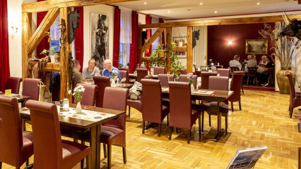A restaurant with wooden beams, red curtains, and a herringbone floor. Tables and chairs are arranged for dining. - Nice Apartment in Klein Upahl (Klein Upahl)