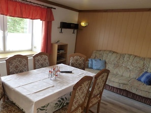 A dining area with a table set for four, a sofa, a bookshelf, and a window with curtains. - Holiday Apartment Family Kreissl (Oberwiesenthal)