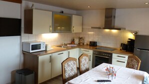 A compact kitchen with a microwave, stove, and sink. There is a dining table with chairs and a trash bin. - Holiday Apartment Family Kreissl (Oberwiesenthal)