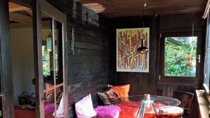 L’intérieur d’un chalet accueillant, avec une porte vitrée donnant sur une terrasse en bois, une table en verre entourée de chaises et un tapis aux couleurs vives.