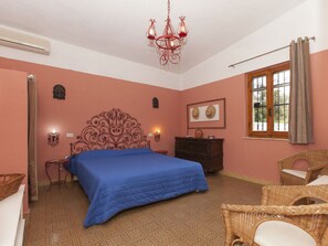 A bedroom with a large bed, a chandelier, a dresser, and a wicker chair.