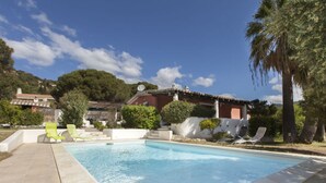 A swimming pool with lounge chairs, a patio area, and a building with a red facade and satellite dish. - Venere Comfortable Holiday Residence (Maracalagonis)