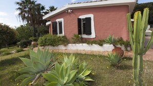 A house with a red exterior and white trim, surrounded by a garden with various plants and a cactus. - Venere Comfortable Holiday Residence (Maracalagonis)