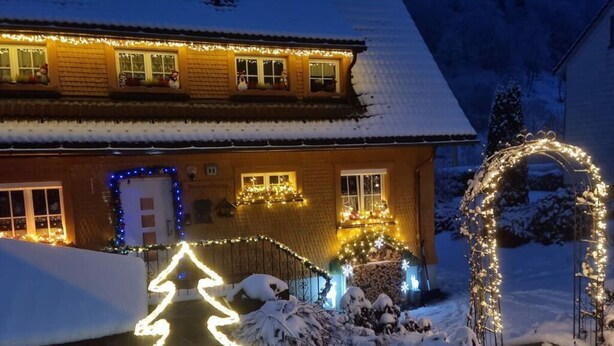 A house with snow-covered surroundings, decorated with lights and a snowman.