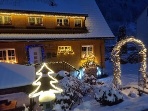 Ett hus omgivet av snötäckt landskap, dekorerat med ljus och en snögubbe.